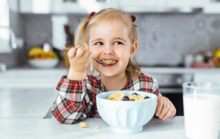 Smiling young girl drinking milk and eat healthy breakfast at the kitchen table
