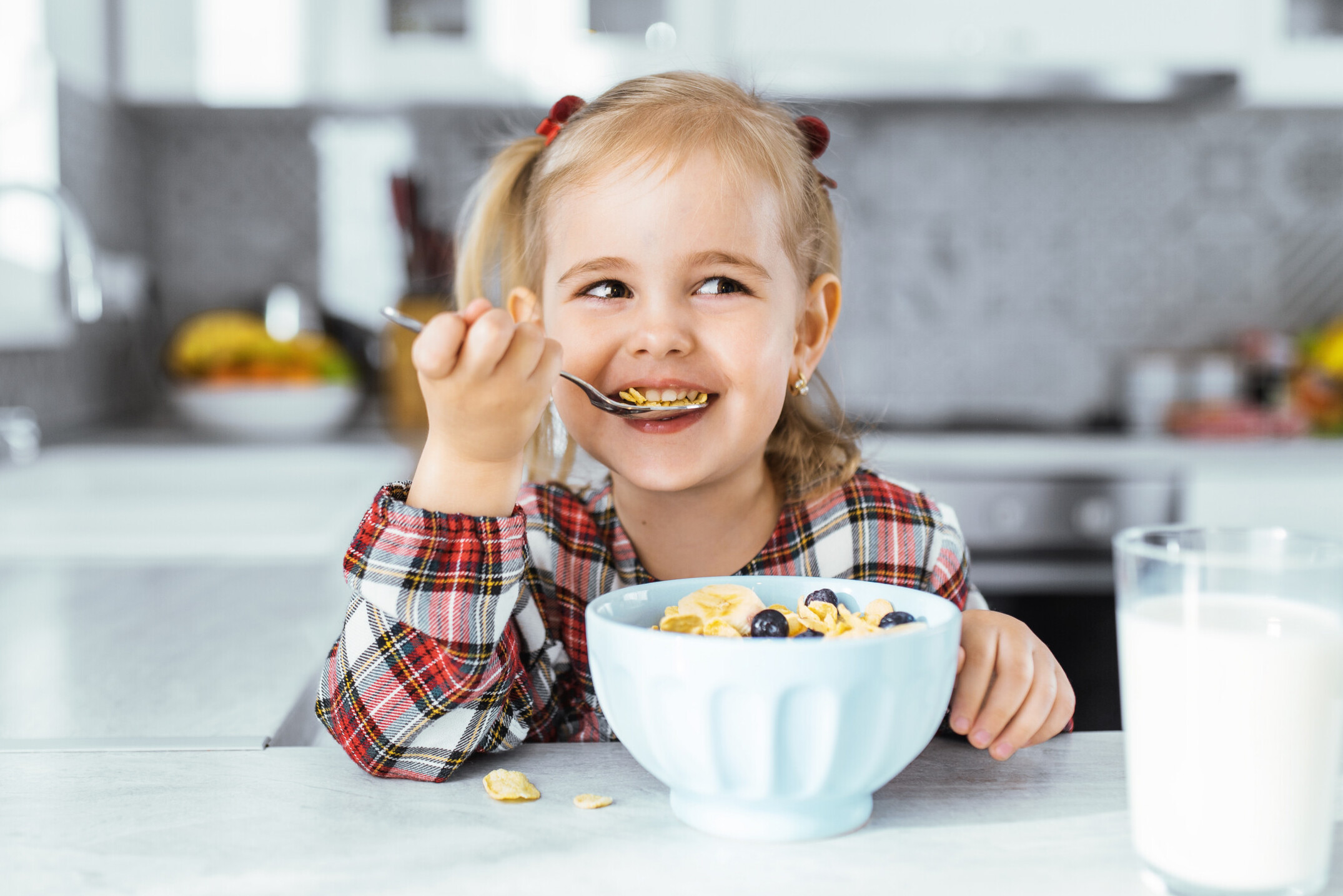 Smiling young girl drinking milk and eat healthy breakfast at the kitchen table